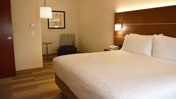 A hotel room with a large bed, a bedside table with a lamp, a chair, and a small table.