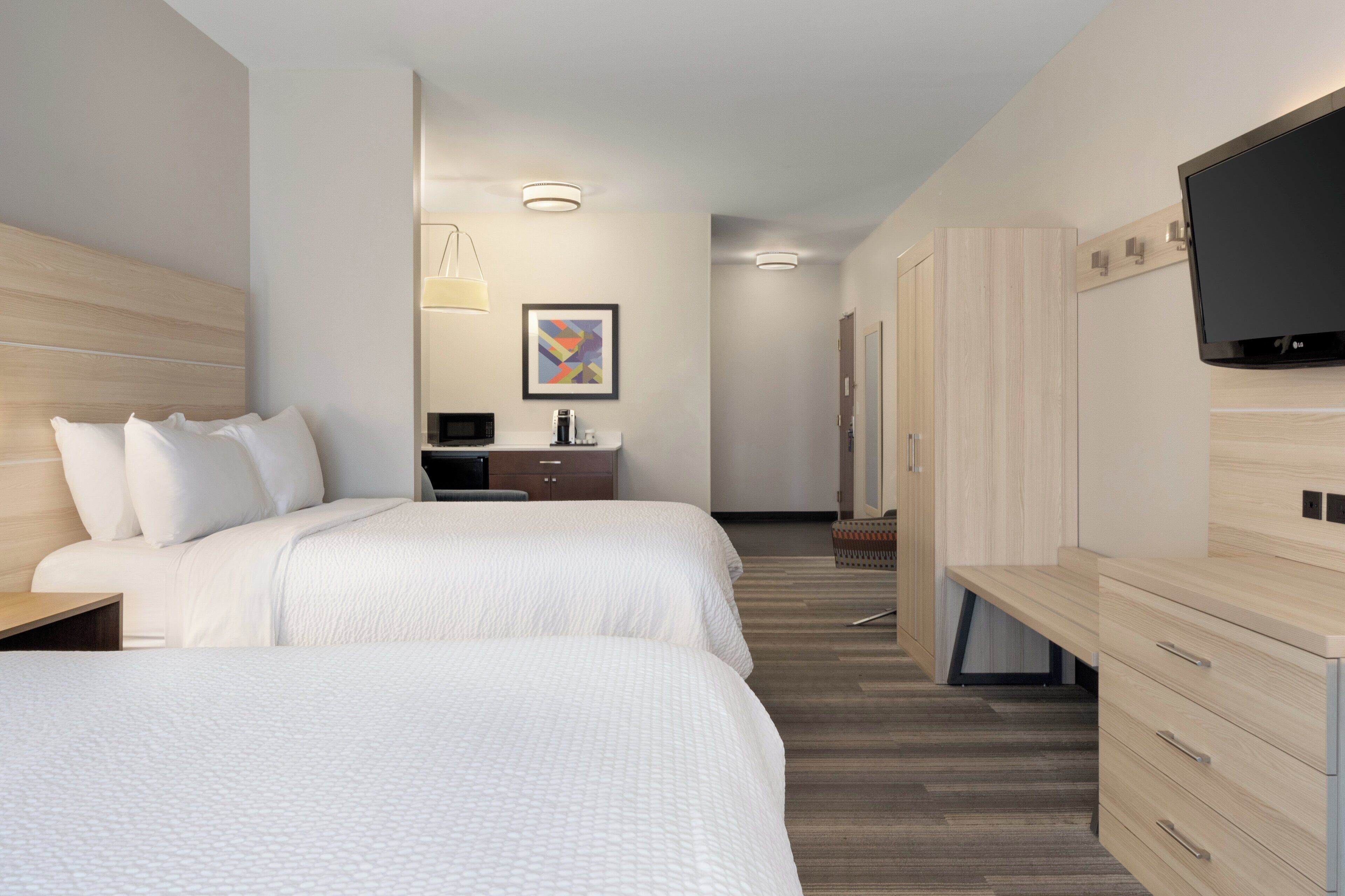 A hotel room with two beds, a TV, a desk, and a bathroom with a shower.