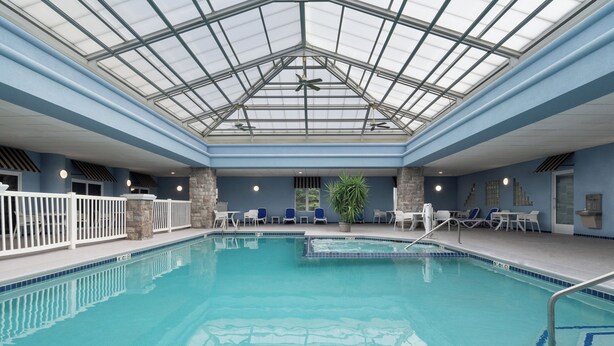 An indoor swimming pool with a glass ceiling, stone pillars, and white lounge chairs. - Holiday Inn Express Hotel & Suites Saginaw by IHG (Saginaw)