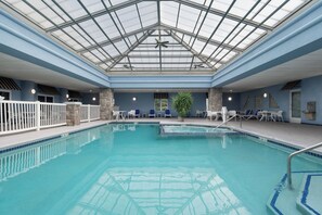 An indoor swimming pool with a glass ceiling, stone pillars, and white lounge chairs. - Holiday Inn Express Hotel & Suites Saginaw by IHG (Saginaw)
