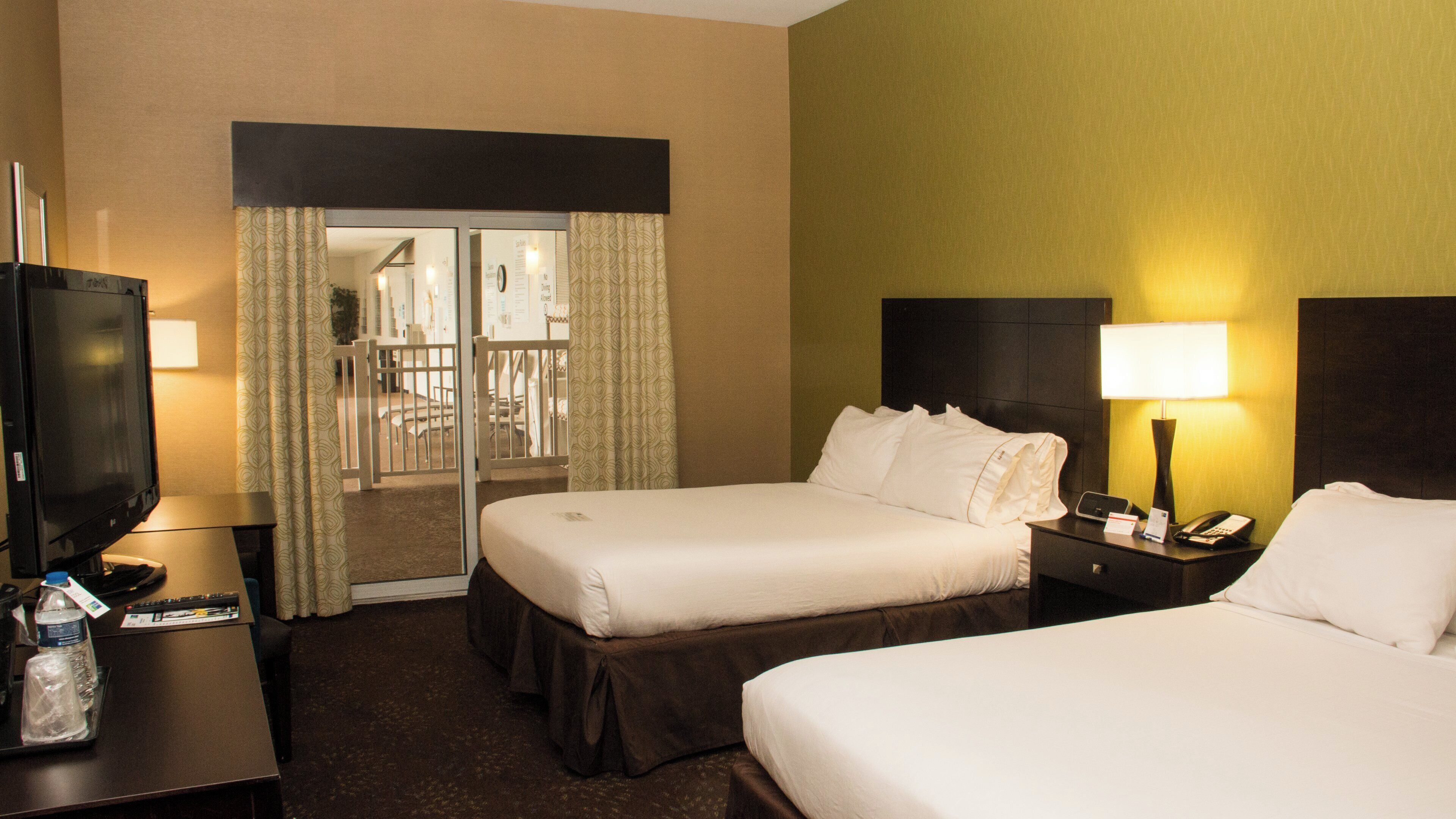 A hotel room with two beds, a television, a desk, and a lamp.