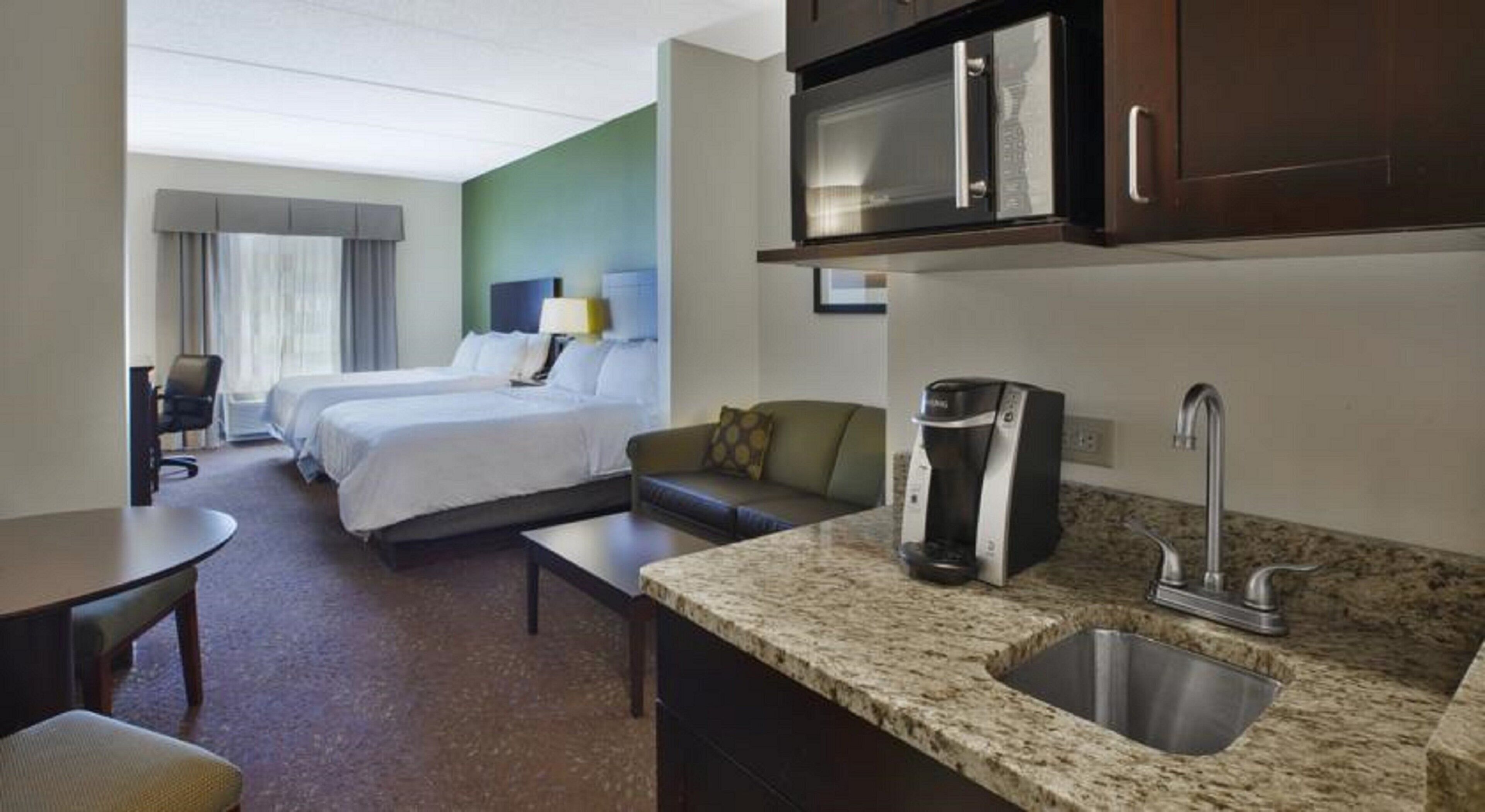 A hotel room with a bed, a sofa, a coffee maker, a microwave, and a sink.