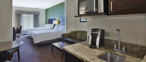 Una habitación de hotel con una cama, un sofá, una cafetera, un microondas y un lavabo.