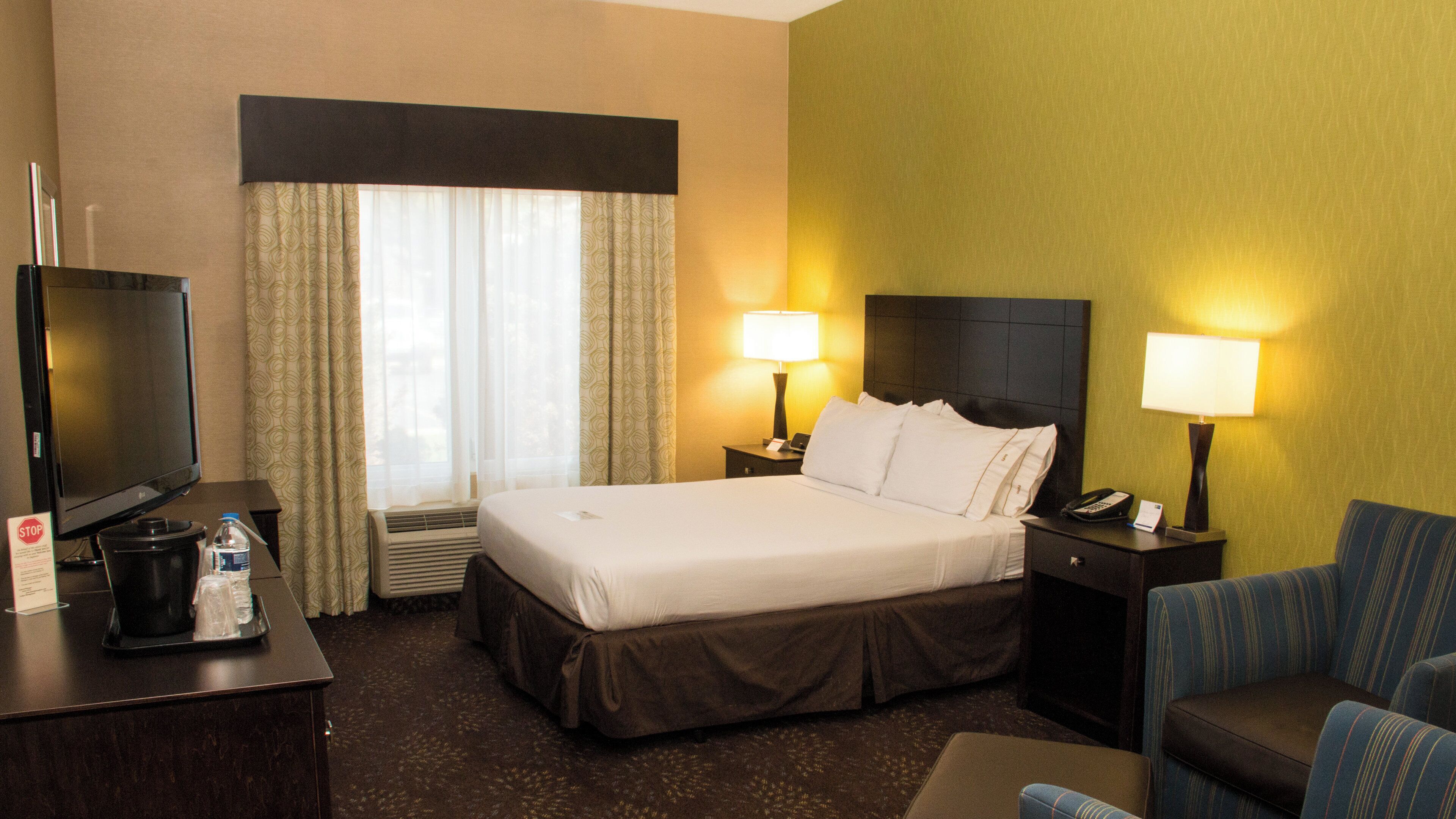 A hotel room with a bed, two bedside lamps, a television, a desk with a water bottle, and a chair.