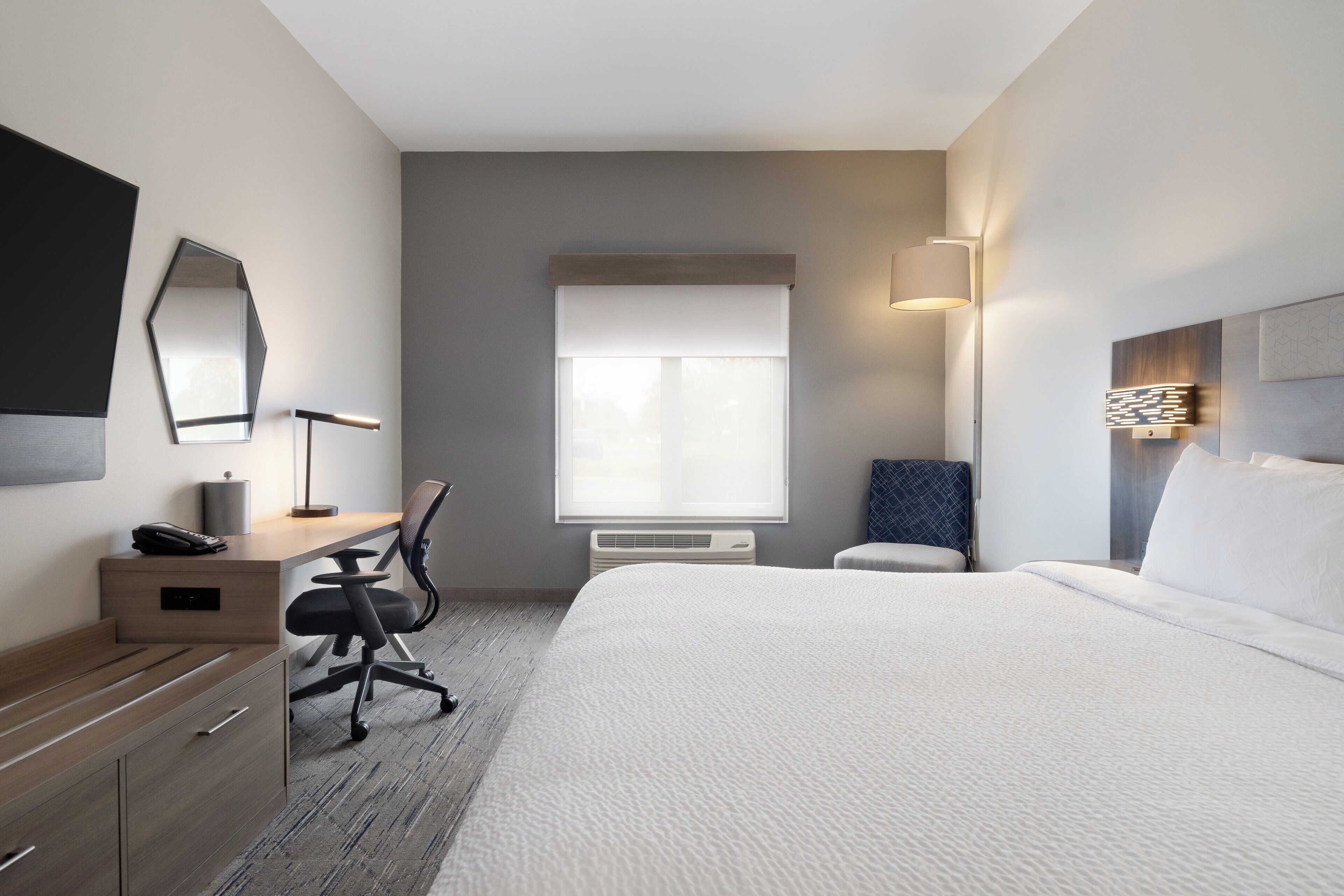 Une chambre d’hôtel moderne dotée d’un grand lit, d’un bureau avec une chaise, d’un téléviseur à écran plat et d’une fenêtre avec des stores.