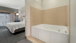 A modern hotel room with a large bed, a separate bathroom with a bathtub, and a window with curtains. - Holiday Inn Express Hotel & Suites Saginaw by IHG (Saginaw)