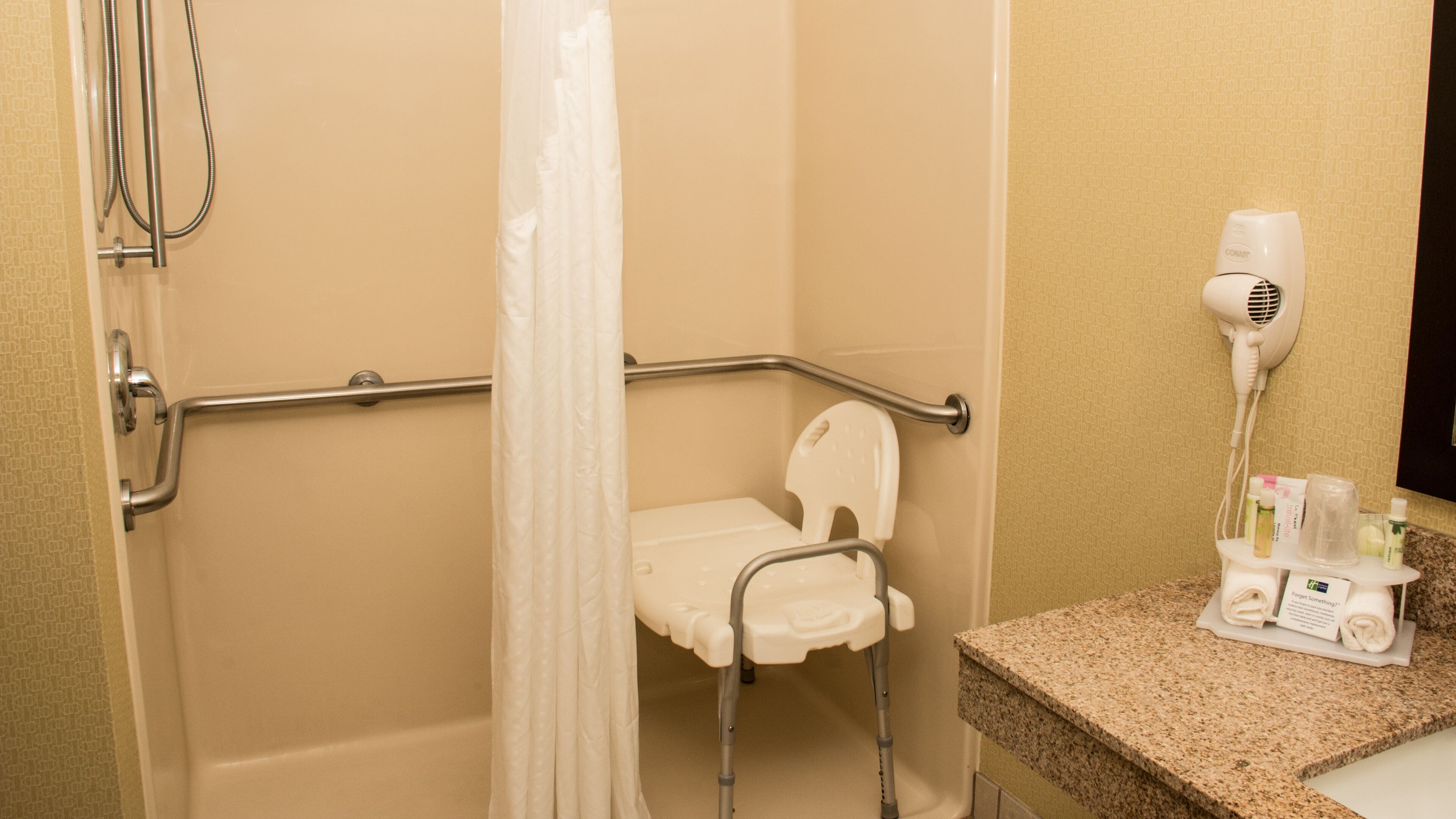 A bathroom with a shower, grab bar, and a hairdryer on the counter.