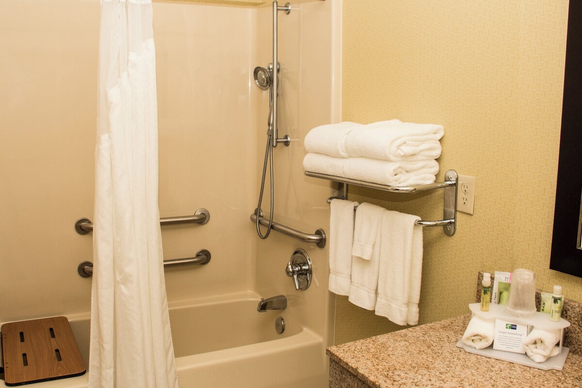 A bathroom with a bathtub, shower, and a towel rack with folded towels.