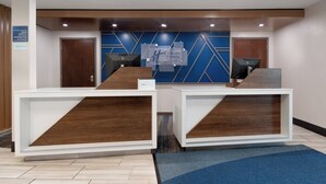 A reception area with two reception desks, a blue wall with geometric patterns, and a sign indicating the hotel name. - Holiday Inn Express Hotel & Suites Saginaw by IHG (Saginaw)