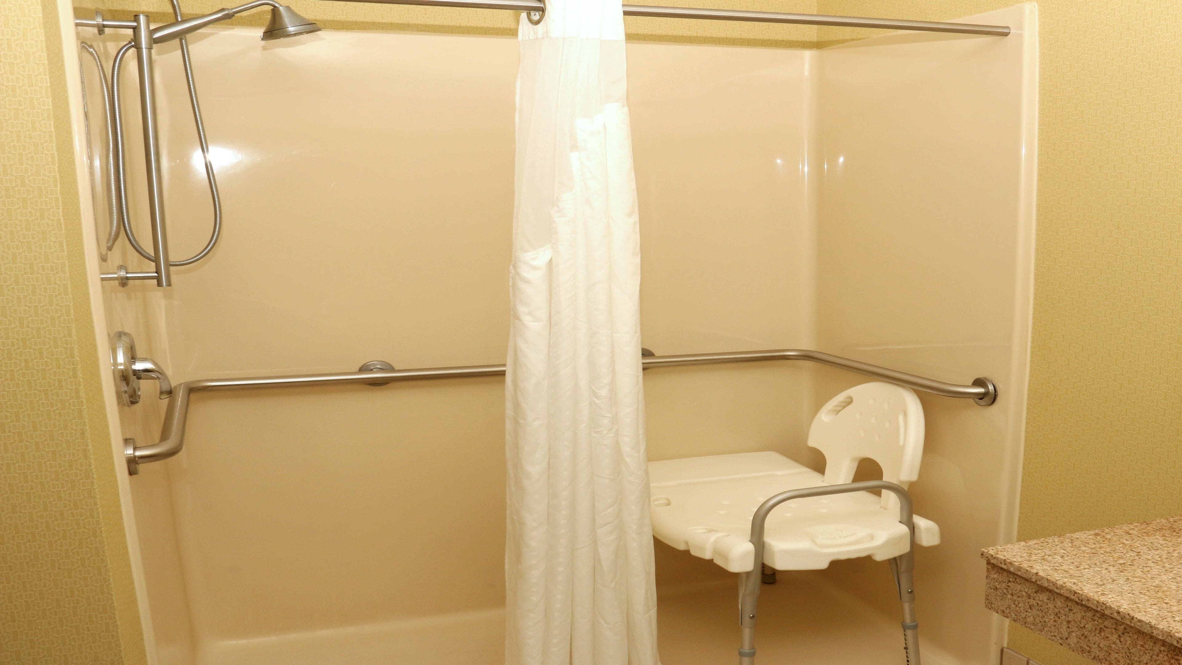 A shower stall with a grab bar, a white shower seat, and a shower curtain.