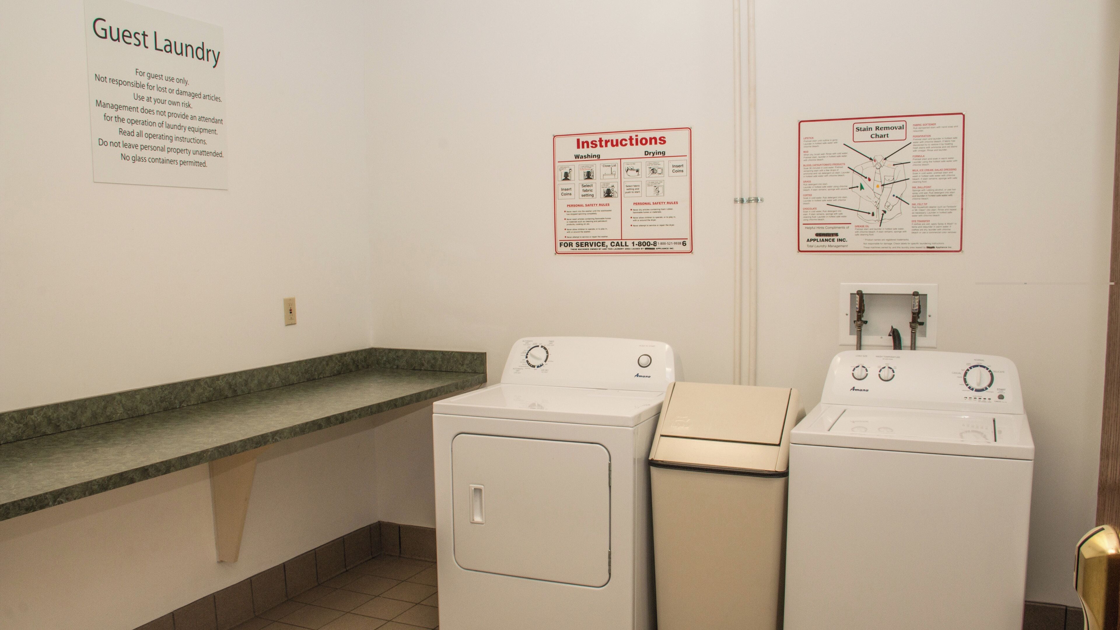 A laundry area with two white washing machines, a sink, and a countertop. There are signs with instructions and safety rules.