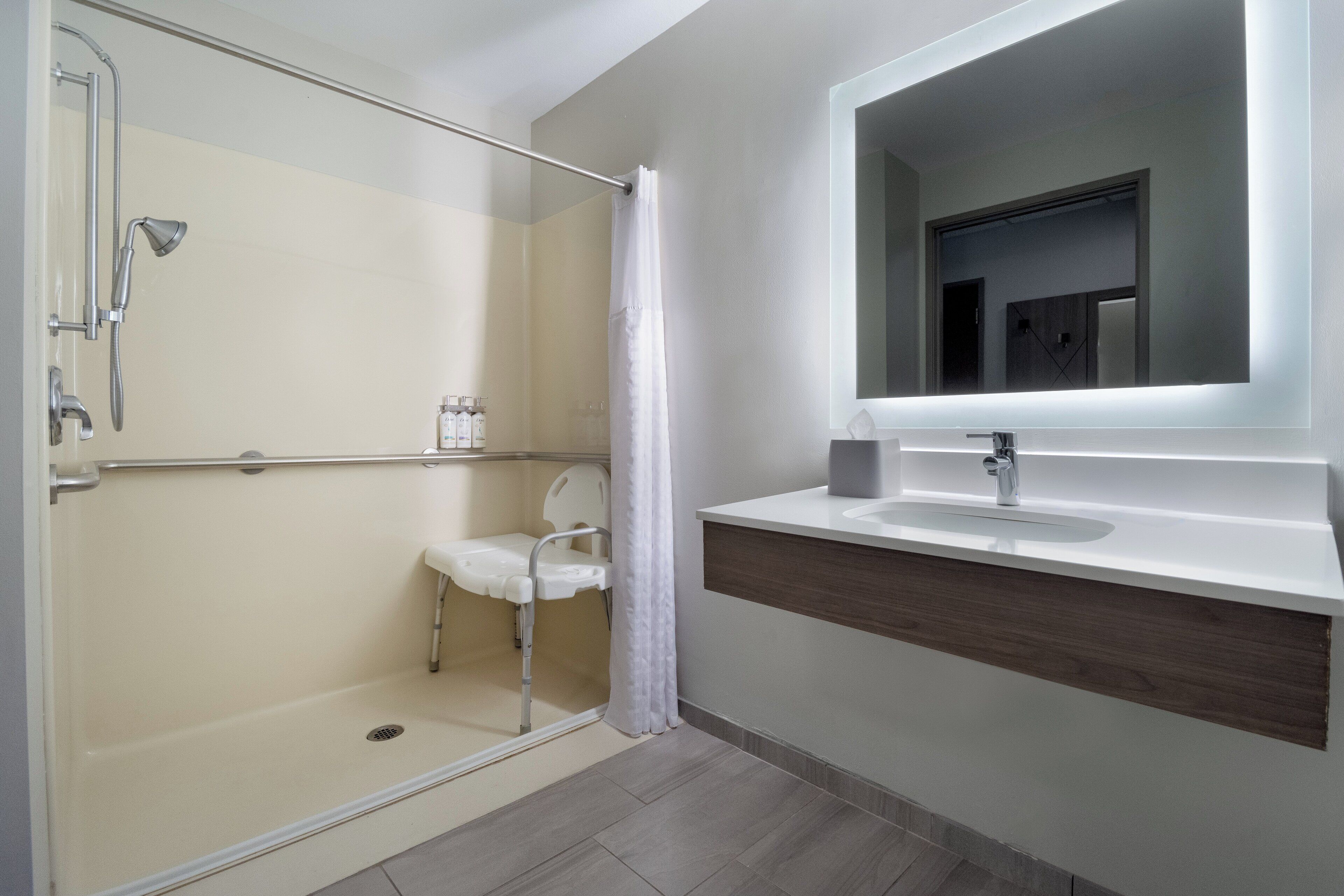 A modern bathroom with a glass shower enclosure, a white sink with a wooden countertop, and a mirror above the sink.