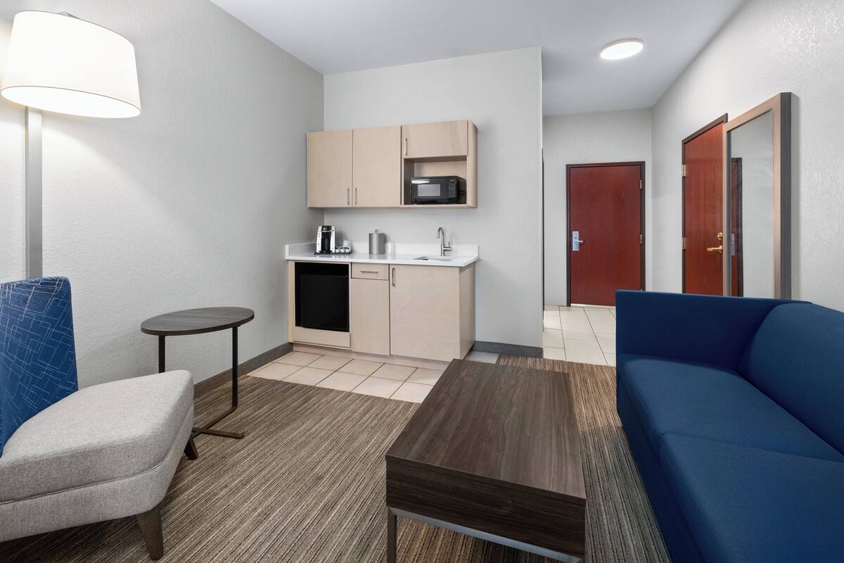 A compact living space with a kitchenette, a sofa, a small table, and a lamp.