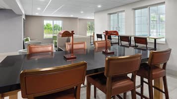 A conference room with a large table and chairs, large windows, and a view of greenery outside.