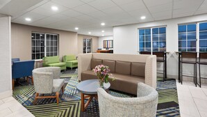 A lobby with a brown sofa, green chairs, a round table, and a patterned rug. - Holiday Inn Express Hotel & Suites Acme-Traverse City by IHG (Williamsburg)
