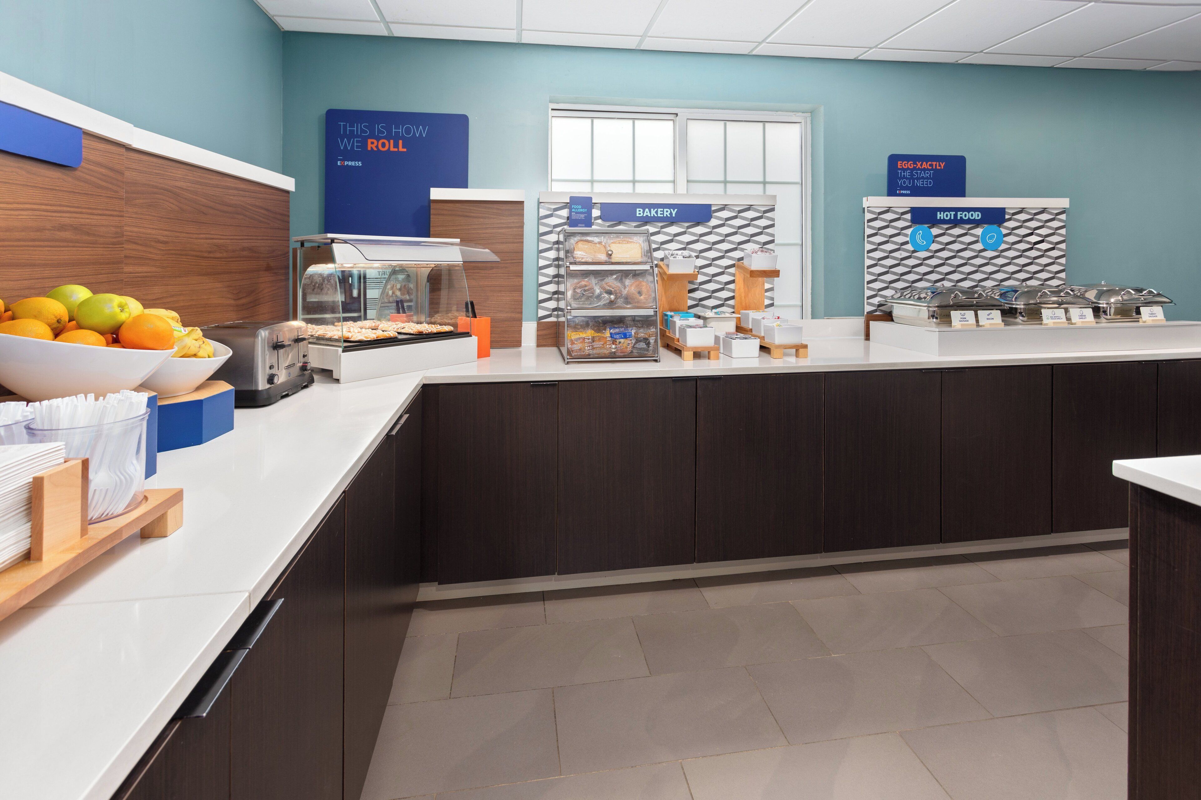 A buffet area with a fruit bowl, a coffee station, and labeled sections for bakery and hot food.
