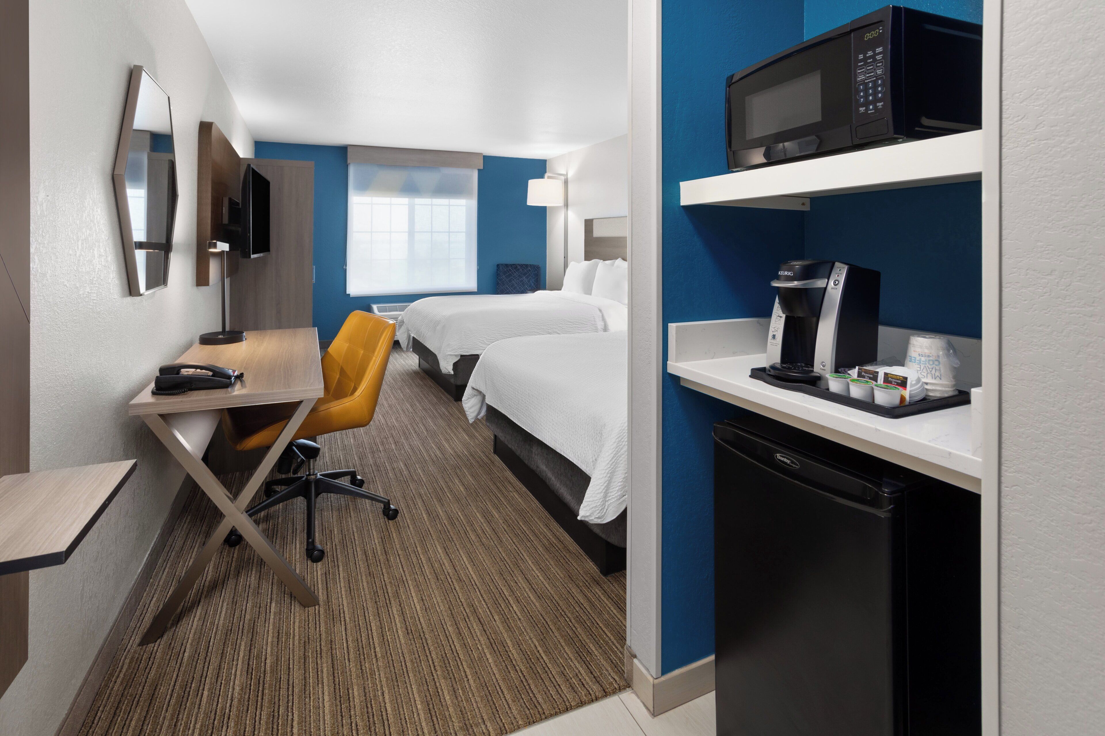 Habitación de hotel con escritorio, dos camas, microondas, cafetera y televisor.