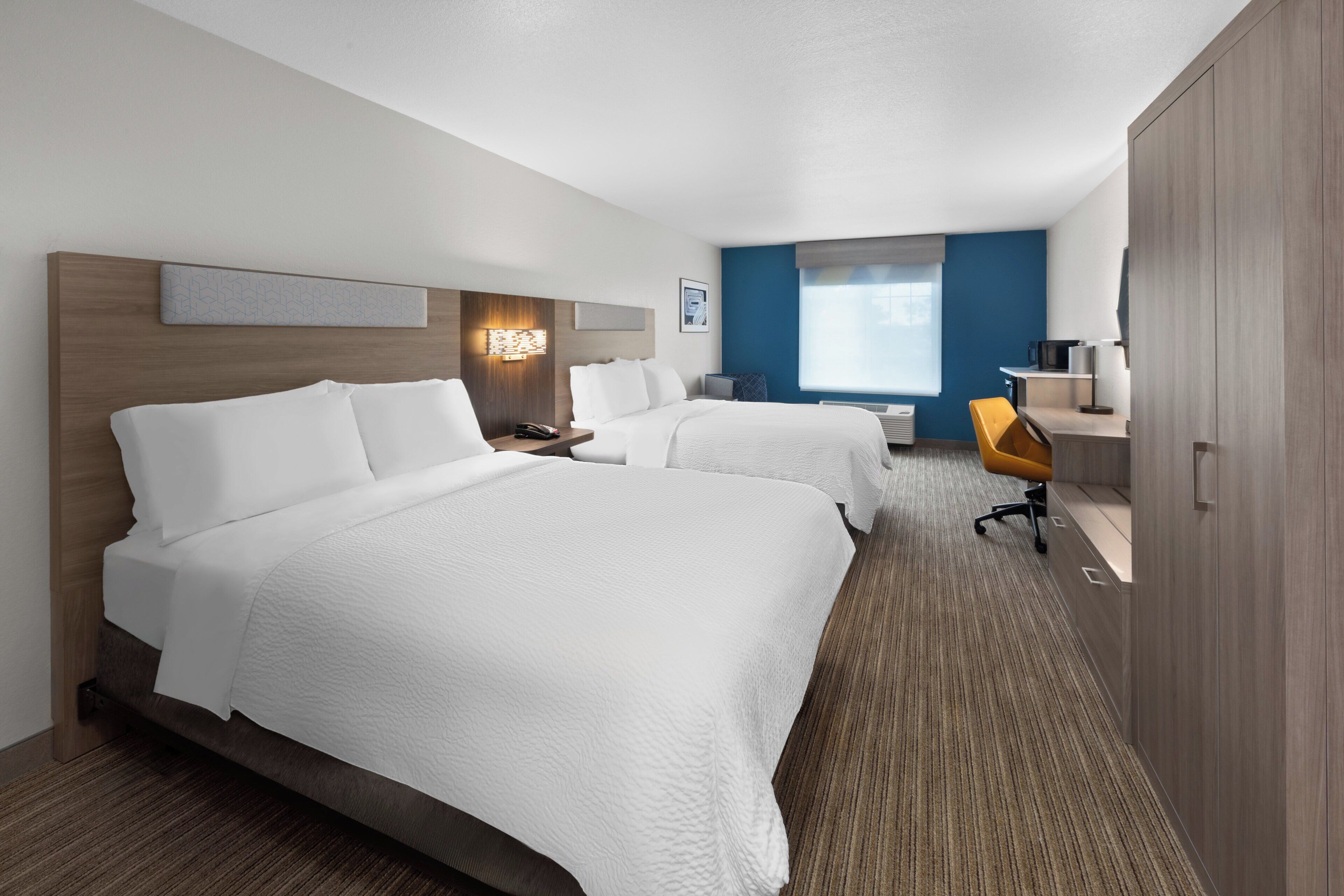 Habitación de hotel con dos camas, un escritorio, una silla y un armario.
