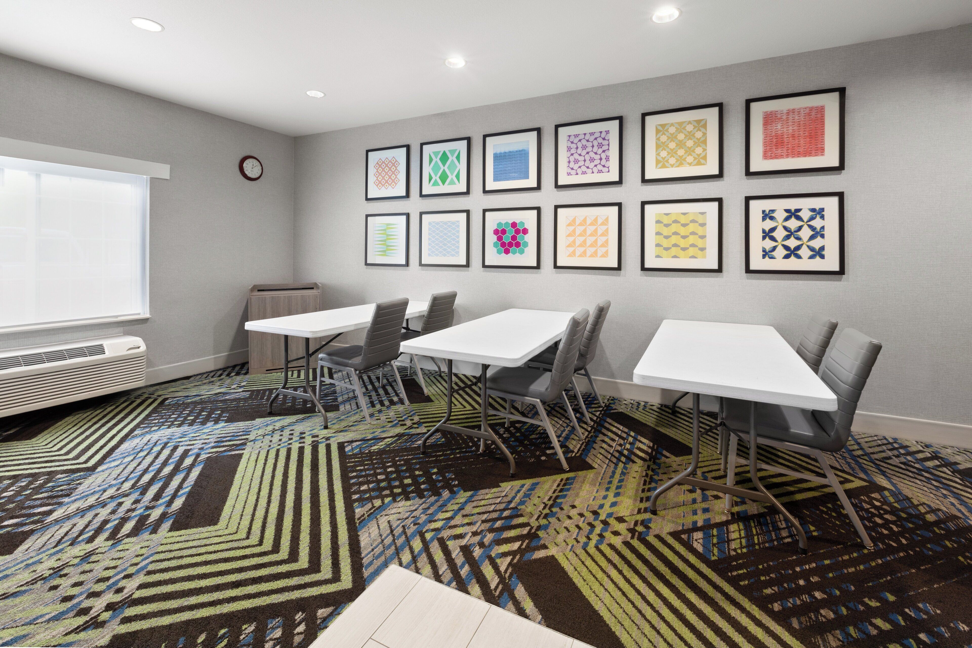 A conference room with white tables and chairs, a patterned carpet, and framed artwork on the wall.