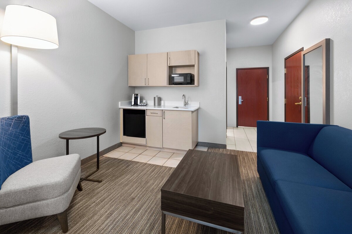 A compact living space with a kitchenette, a sofa, a small table, and a lamp.