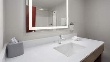 A modern bathroom with a white sink, a large mirror, and a towel dispenser.