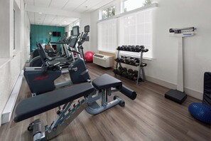 A gym with treadmills, a bench press, dumbbells, and a red exercise ball.