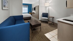A hotel room with a blue sofa, a small table, a bed, a chair, a desk, and a lamp. - Holiday Inn Express Hotel & Suites Acme-Traverse City by IHG (Williamsburg)