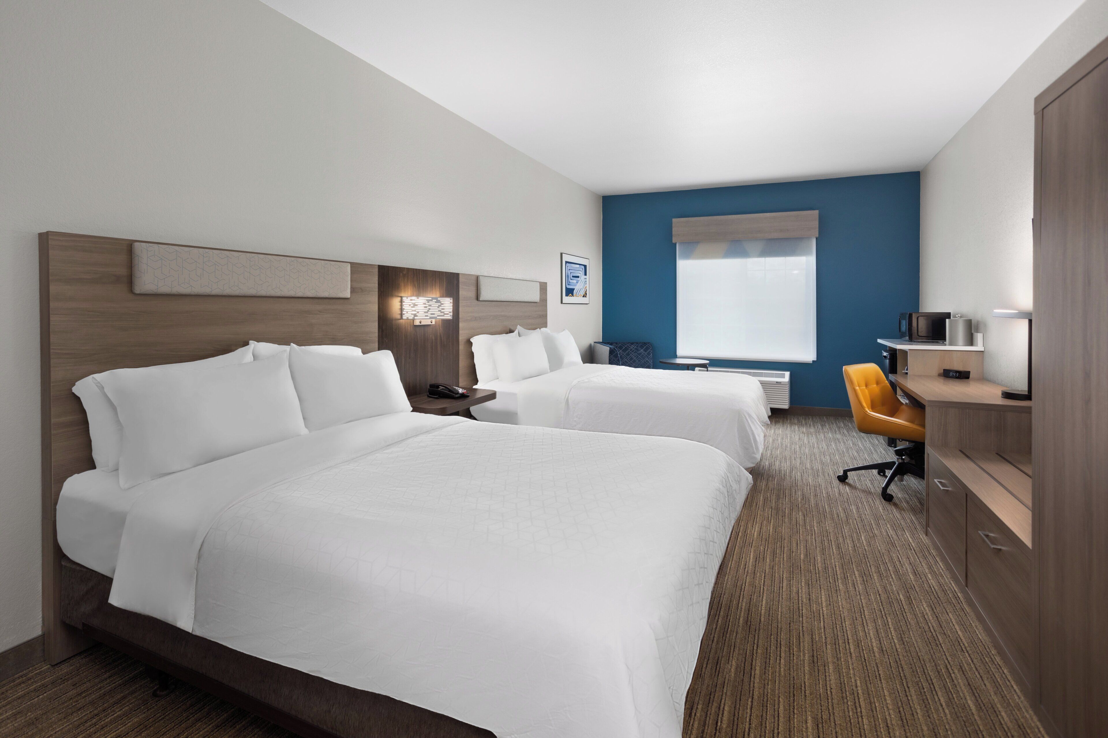 Een hotelkamer met twee bedden, een bureau, een stoel, een koffiezetapparaat en een raam met jaloezieën.