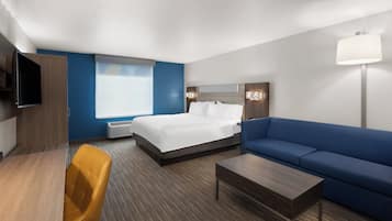 A hotel room with a bed, a sofa, a desk, a chair, a TV, and a lamp.