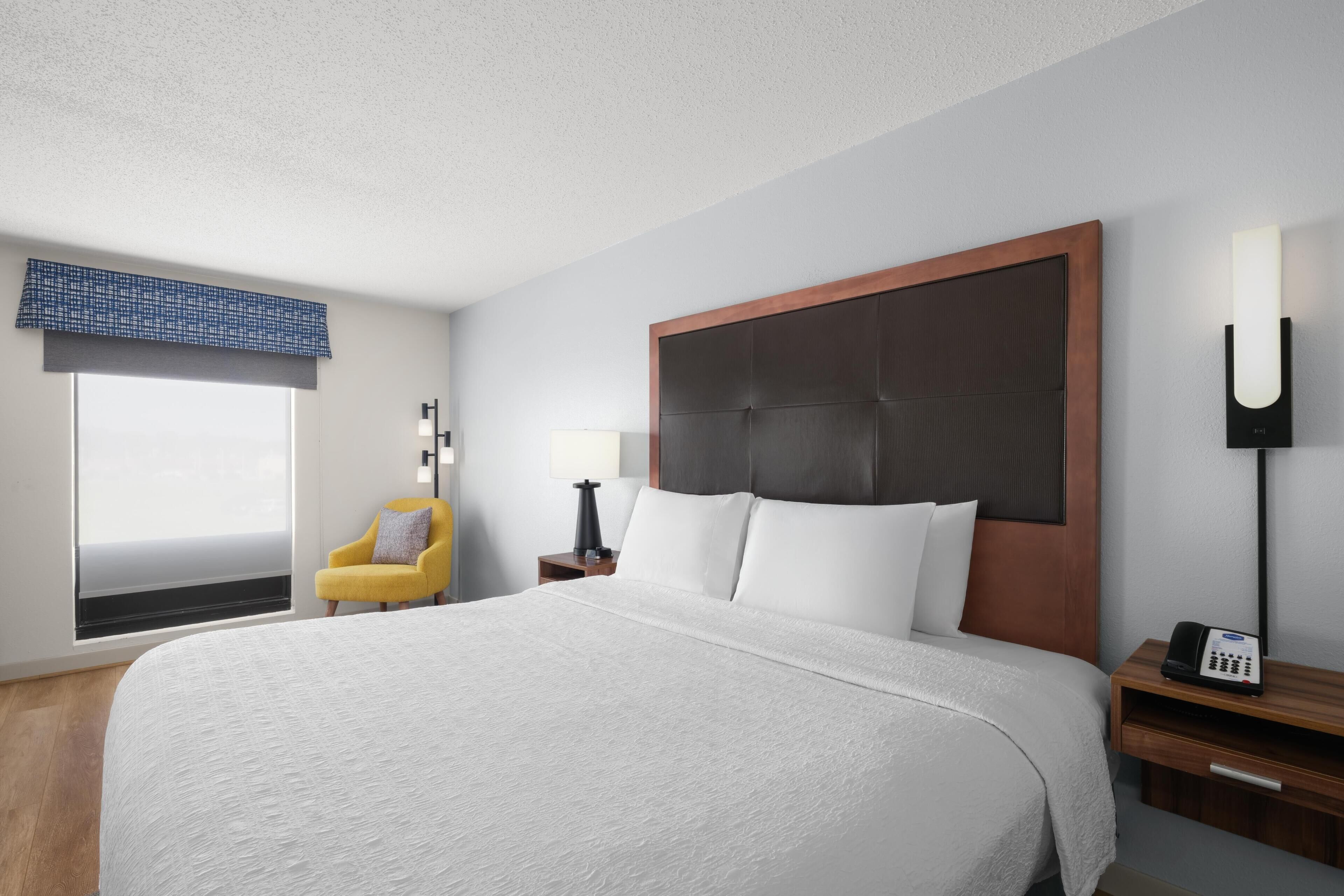 A hotel room with a large bed, a bedside table with a lamp, a phone, and a chair.