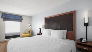 A hotel room with a large bed, a bedside table with a lamp, a phone, and a chair.