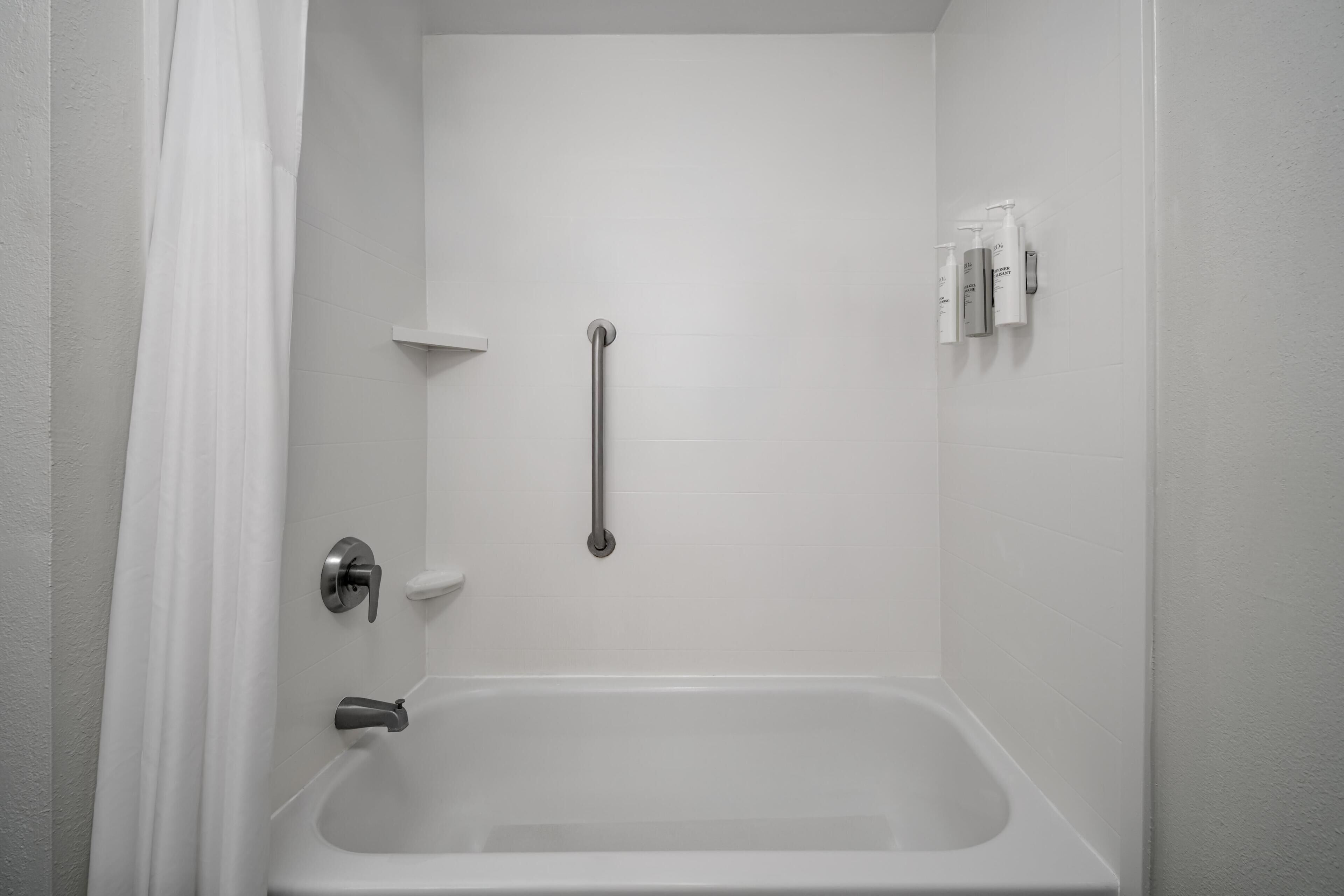 Un baño blanco con bañera, barra de apoyo, perchero y dispensador de jabón.