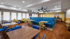 Un interior de restaurante moderno con techos altos, iluminación empotrada y una variedad de opciones de asientos, incluyendo mesas y sofás.