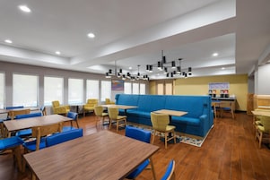 Un interior de restaurante moderno con techos altos, iluminación empotrada y una variedad de opciones de asientos, incluyendo mesas y sofás.