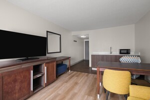 Una habitación de hotel moderna con televisión de pantalla plana, muebles de madera, una mesa de comedor con sillas, un microondas y una pequeña kitchenette.