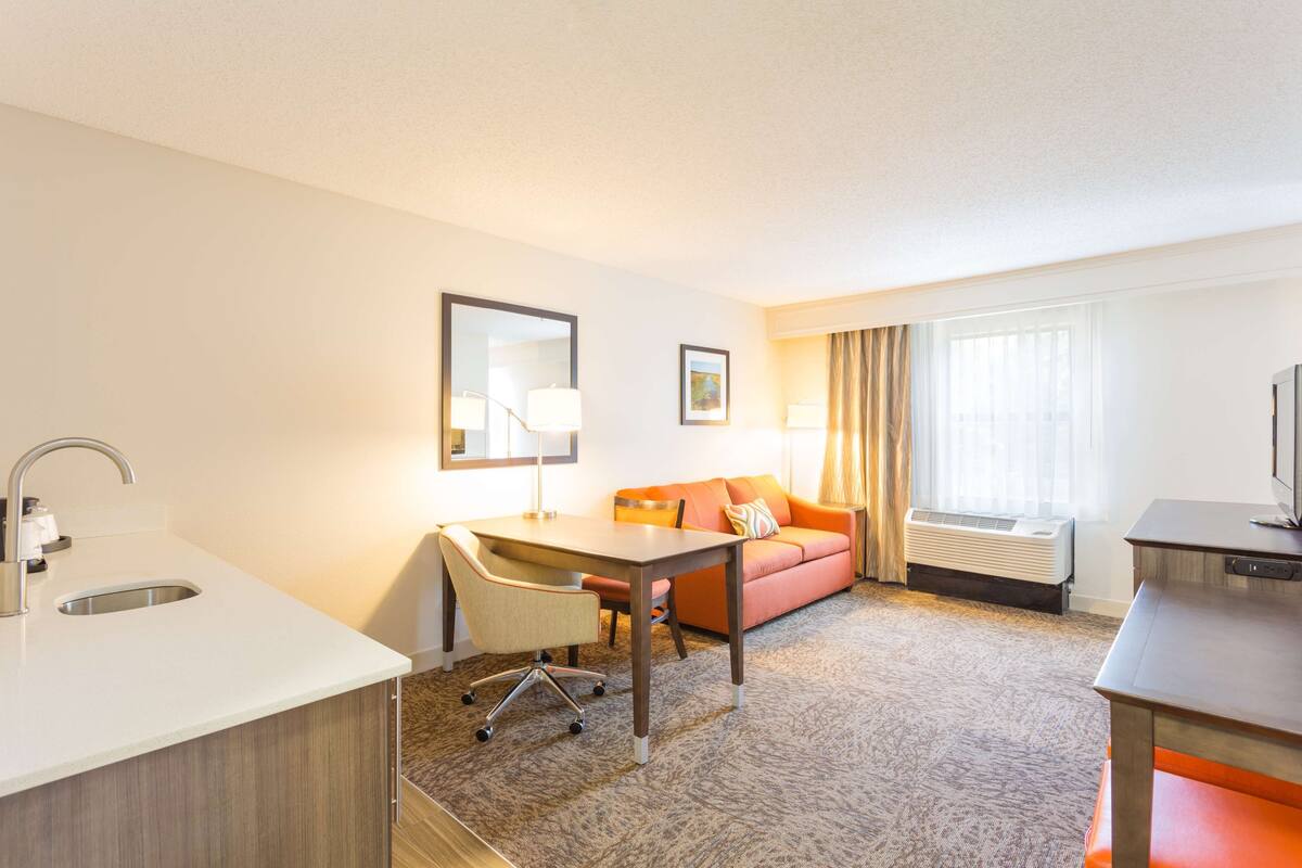 Una habitación de hotel con kitchenette, un sofá, un escritorio y un ventanal grande.