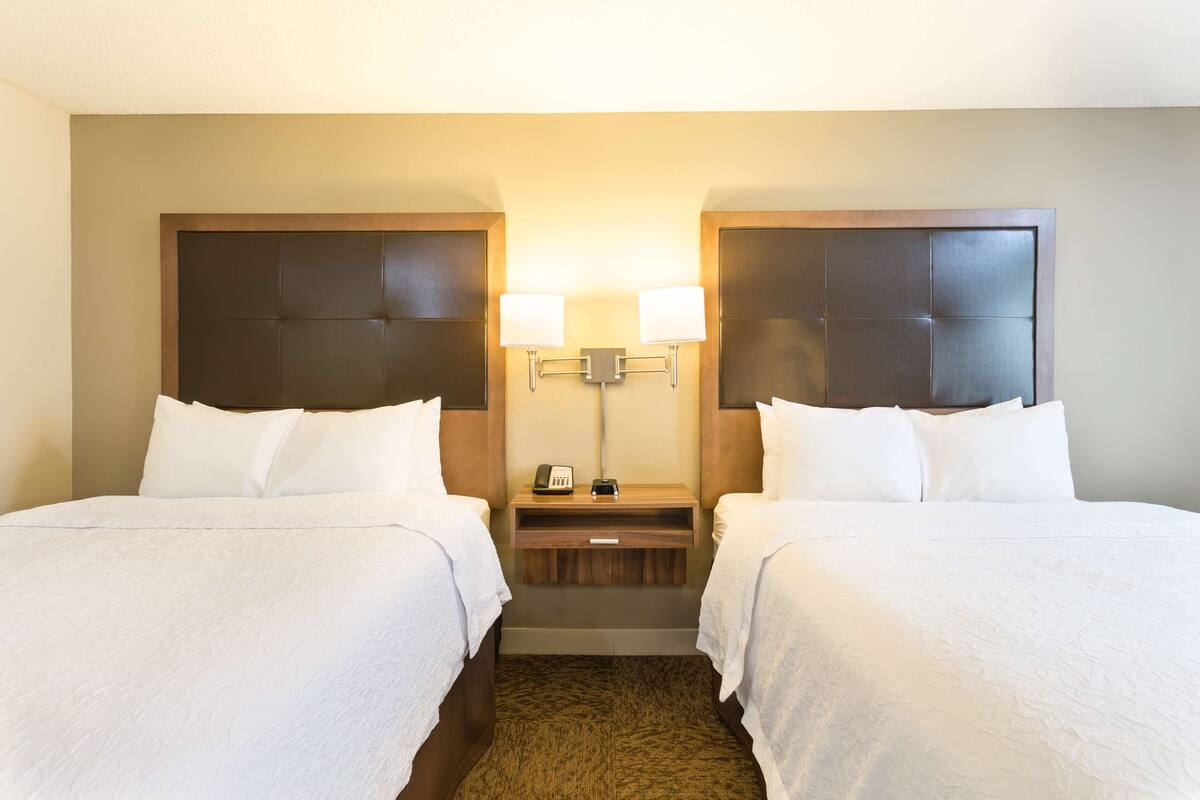 Habitación de hotel con dos camas, una mesita de noche con lámpara y una pequeña mesa entre las camas.