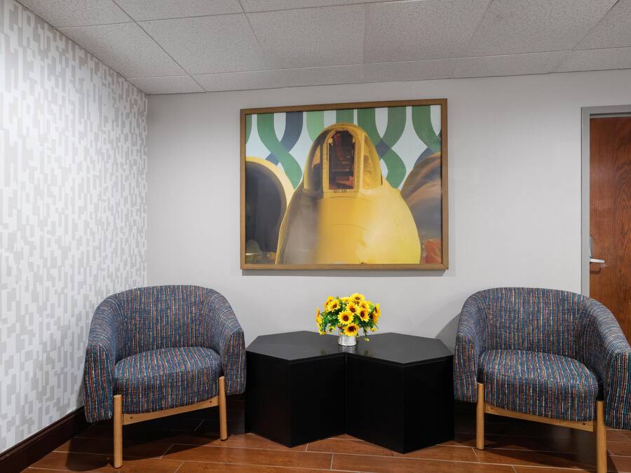 A room with two patterned chairs, a black table, and a painting on the wall.
