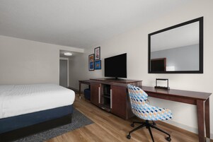 A hotel room with a bed, a desk, a chair, a television, and a mirror.