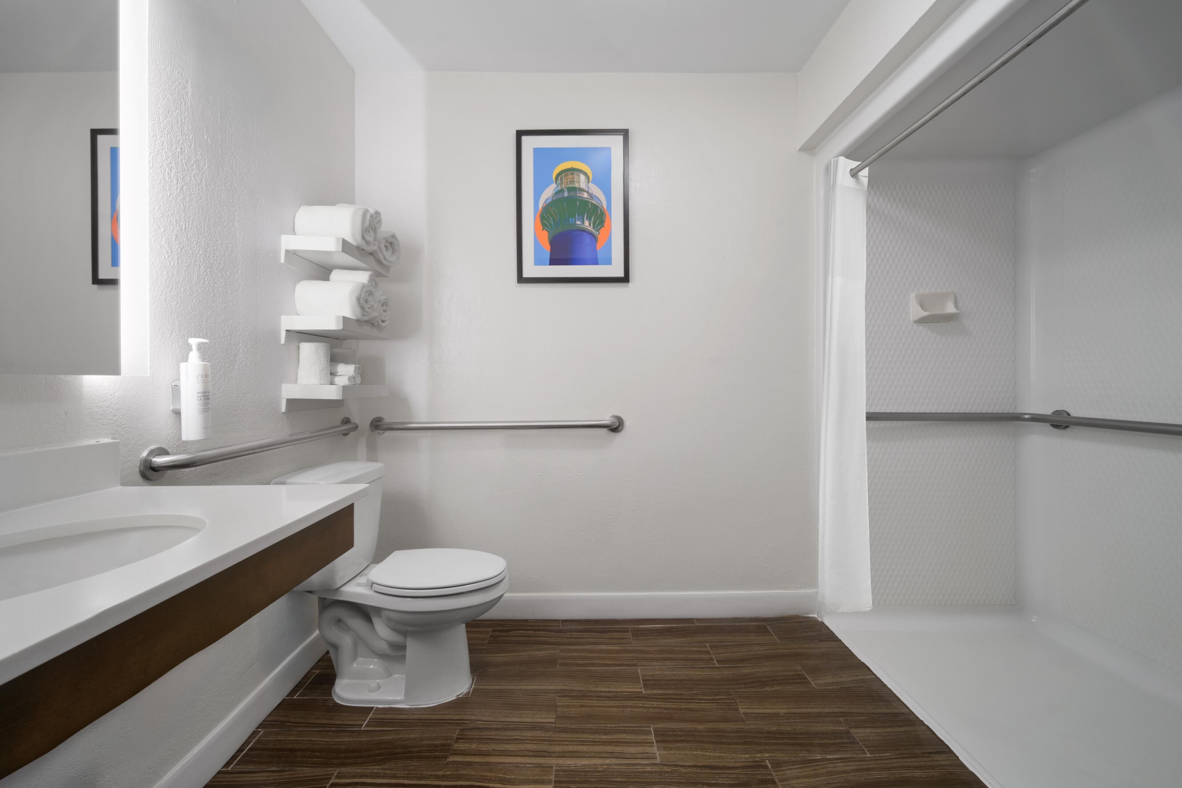 A modern bathroom with a toilet, a sink, a shower area, and a framed picture on the wall.