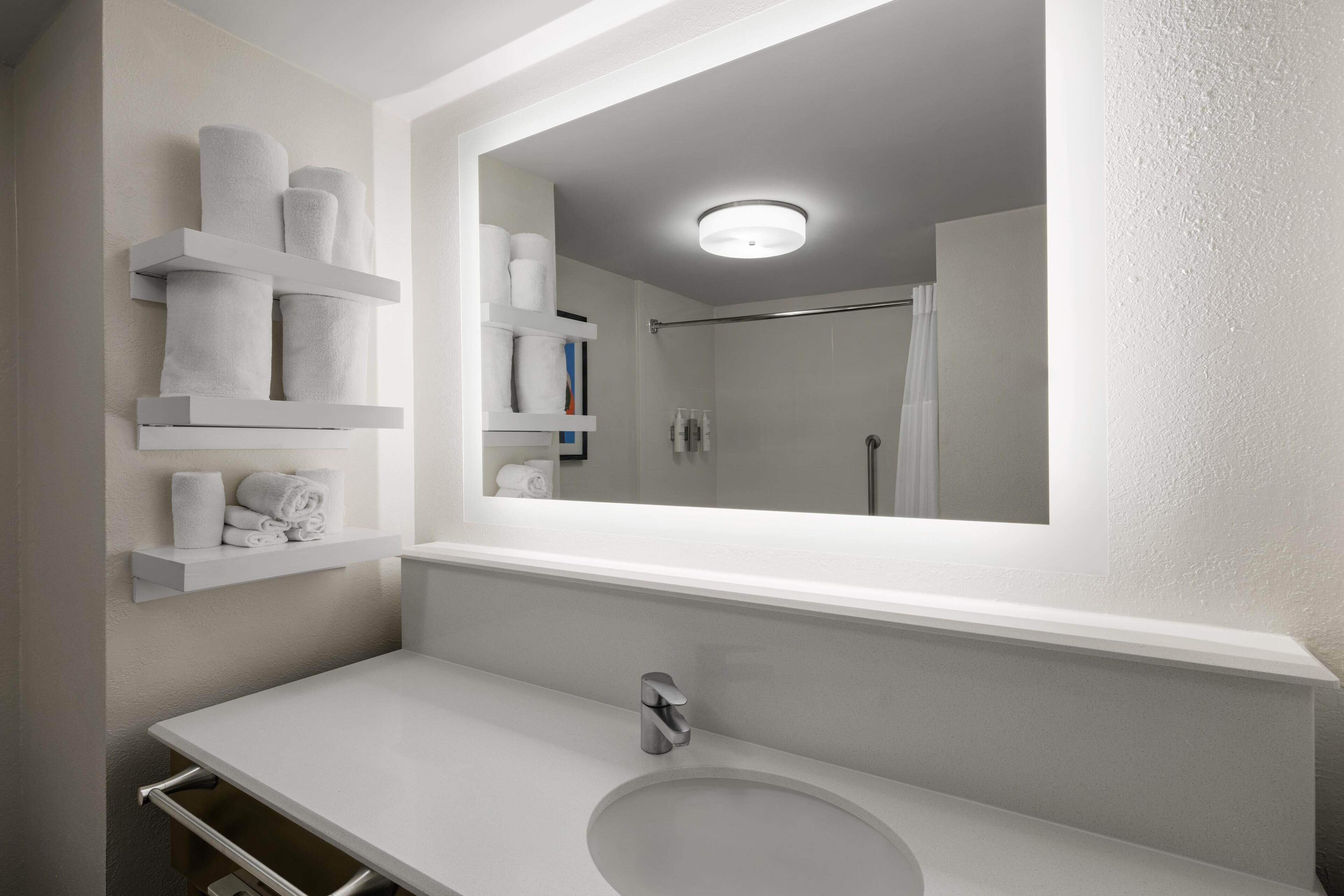 A bathroom with a white sink, a mirror, and shelves holding towels.