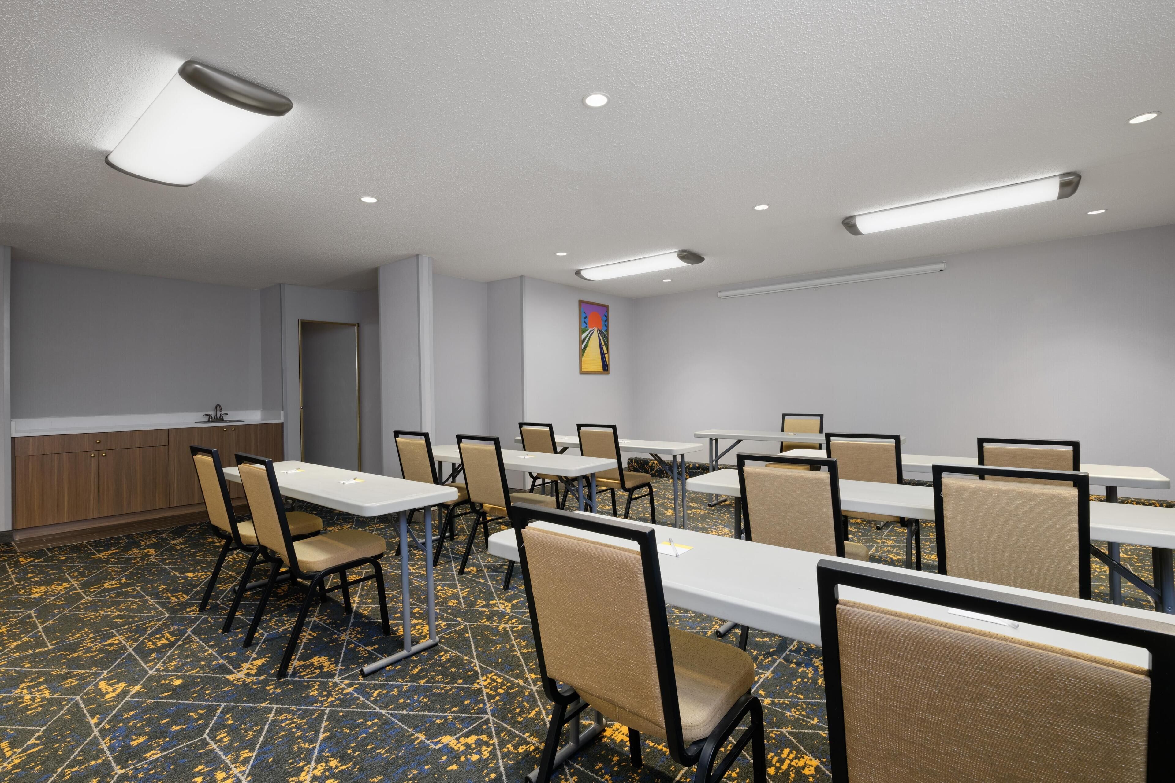 Uma sala de conferências com mesas, cadeiras, uma copa e um quadro na parede.