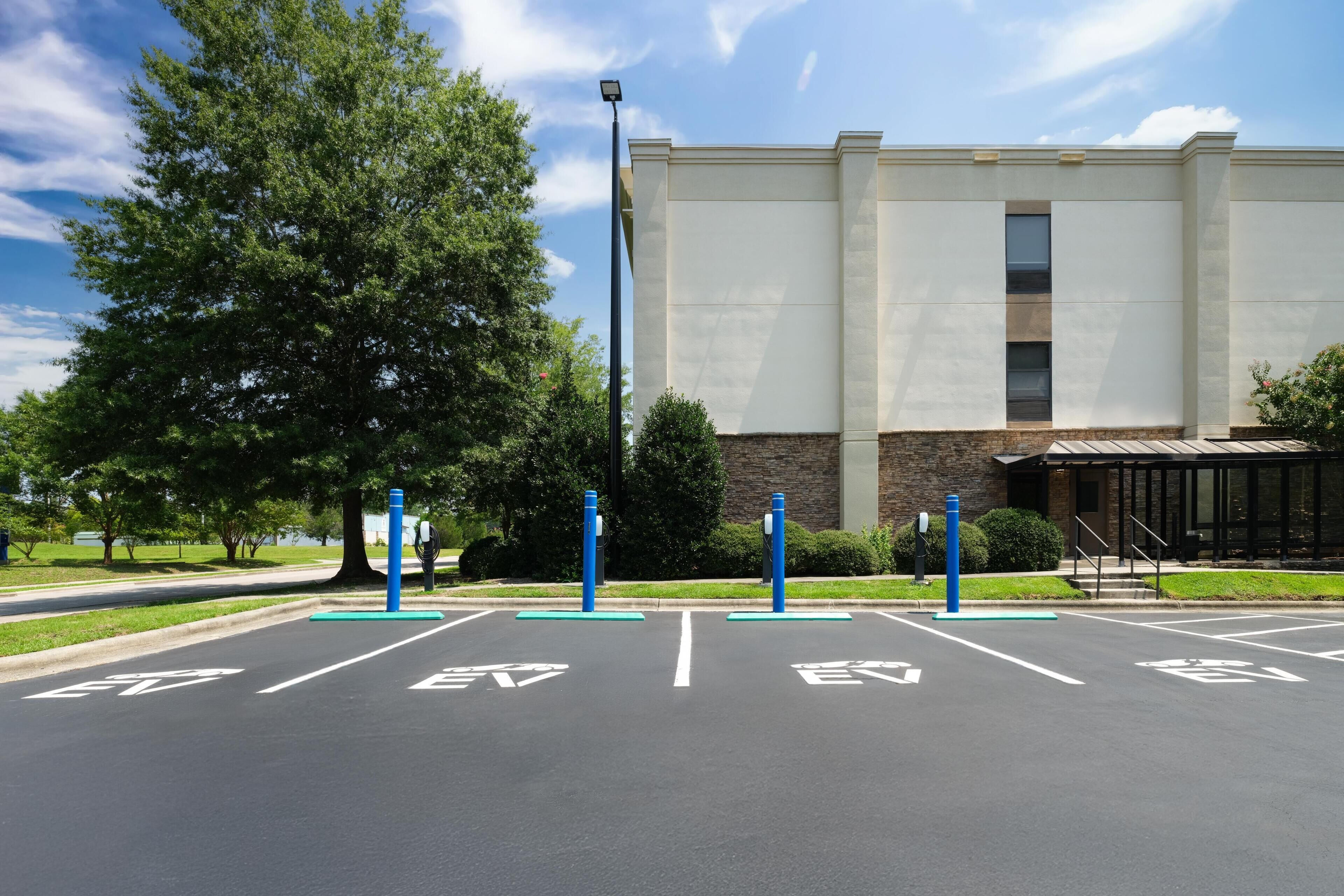 A parking lot with electric vehicle charging stations, a building with a modern design, and a clear sky.