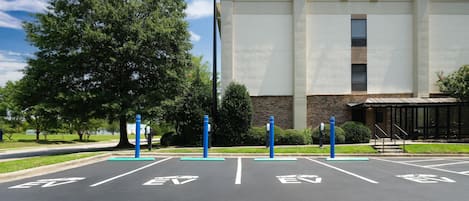 A parking lot with electric vehicle charging stations, a building with a modern design, and a clear sky.