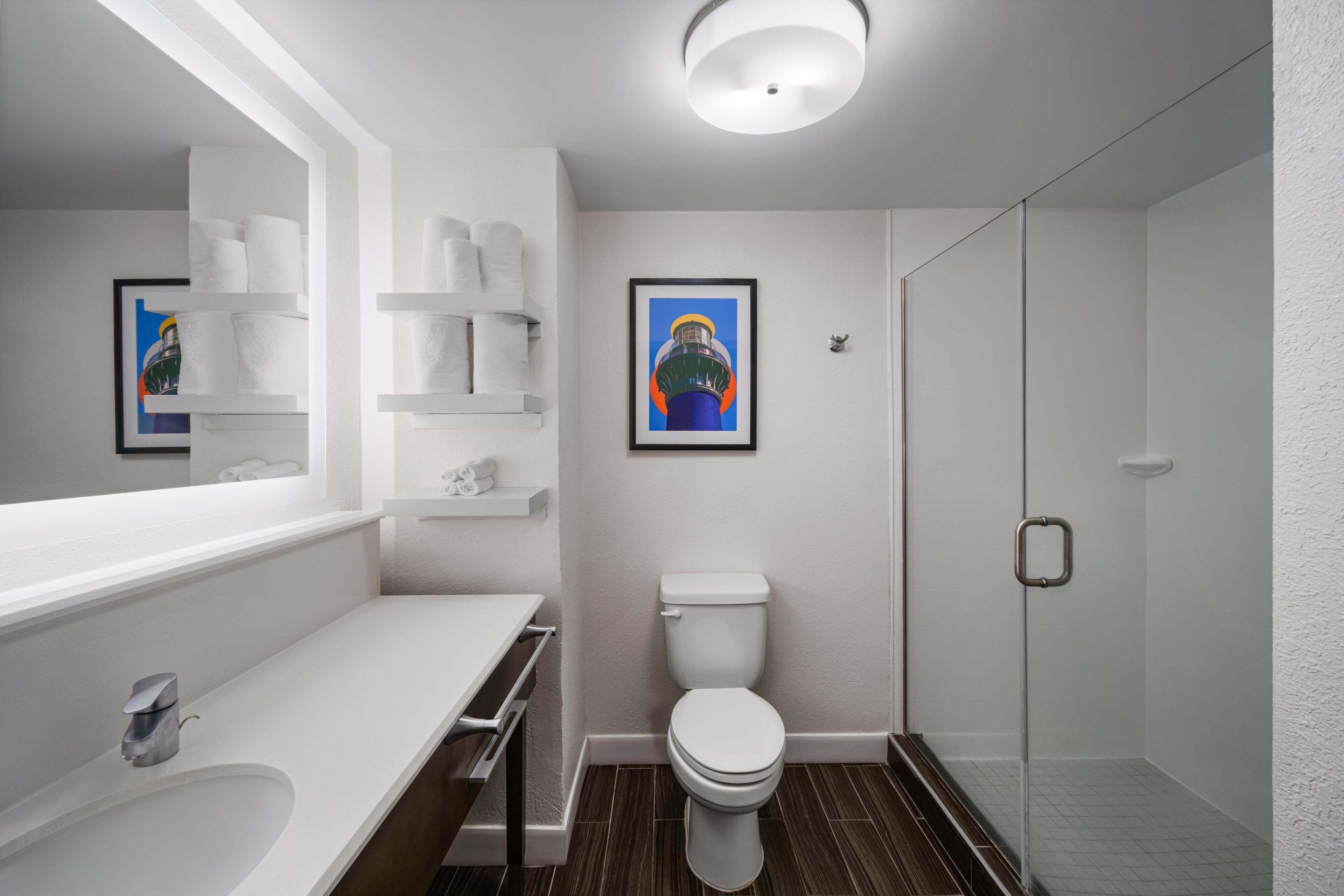 Une salle de bain moderne avec des toilettes, un lavabo et une douche. On y trouve des serviettes et un tableau encadré accroché au mur.