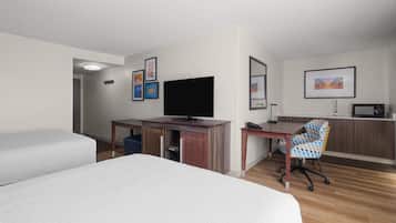 Habitació d'hotel amb dos llits, una taula de treball, un televisor de pantalla plana, una cadira i un microones.