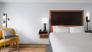 A hotel room with a bed, a chair, a bedside table, a lamp, and a wall-mounted phone.