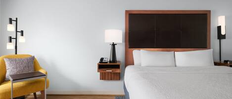 Une chambre d’hôtel équipée d’un lit, d’une chaise, d’une table de chevet, d’une lampe et d’un téléphone fixé au mur.