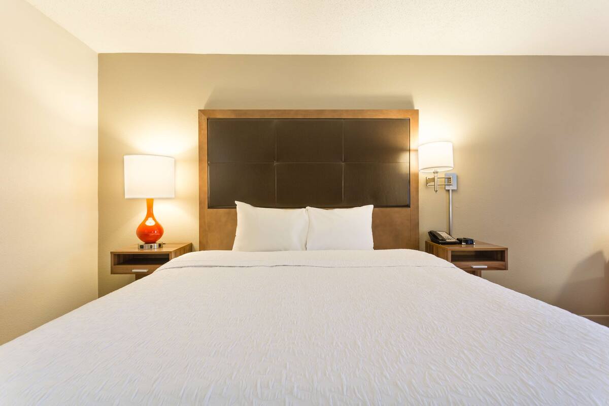 Una habitación de hotel con una cama grande, dos mesitas de noche, un cabecero de madera y dos lámparas de pared.