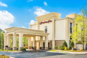 A hotel entrance with a covered patio, a clear sky, and landscaped surroundings.